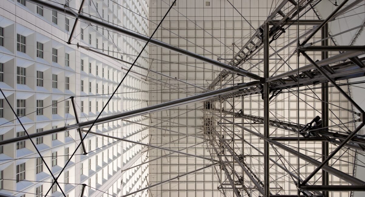 Photographie d'architecture en contre-plongée à 90 degrés de la structure métallique et des câbles sous la Grande Arche de la Défense à Paris.