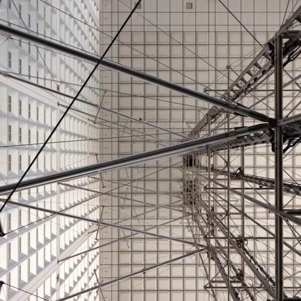 Photographie d'architecture en contre-plongée à 90 degrés de la structure métallique et des câbles sous la Grande Arche de la Défense à Paris.