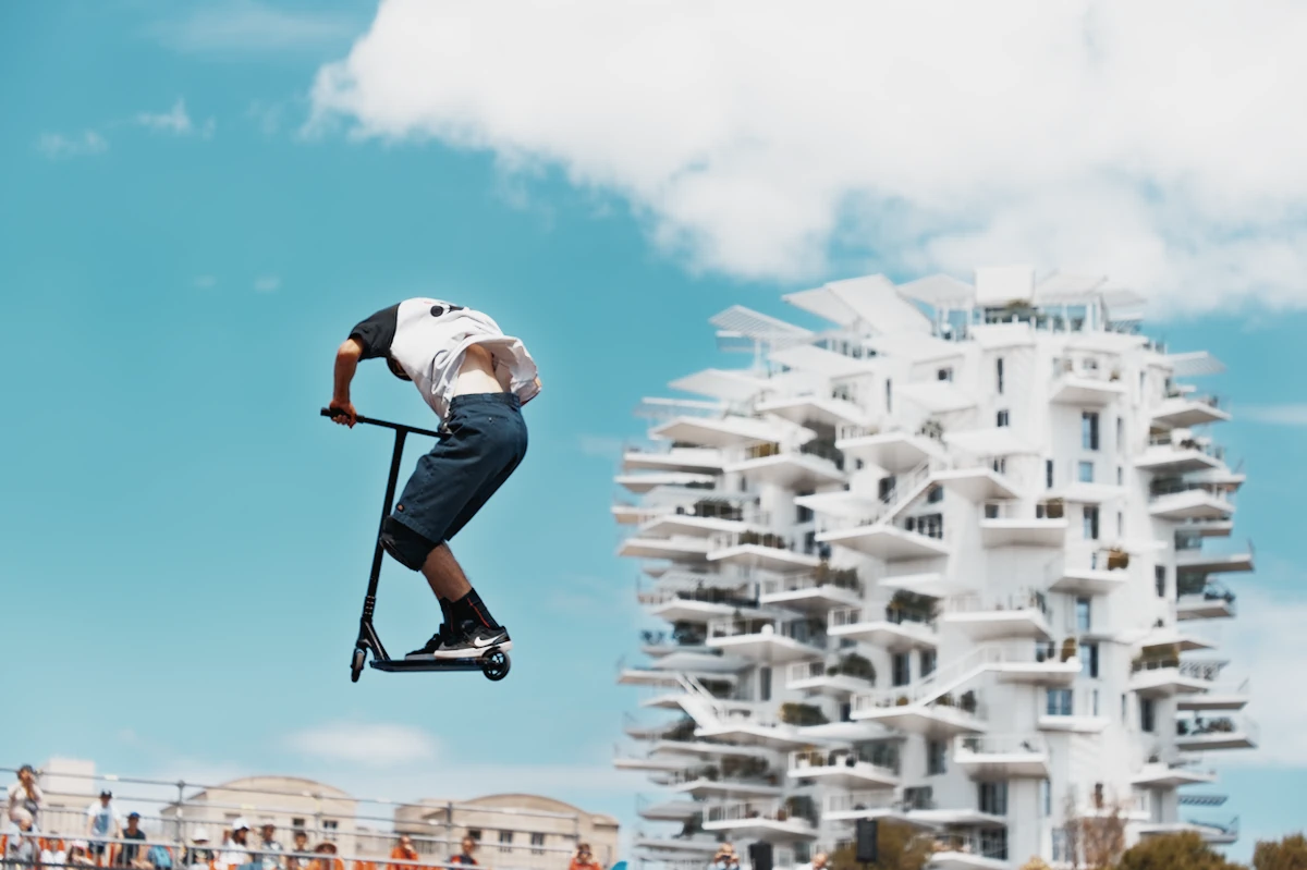 Photographie d'un rider de trottinette professionnel en plein saut au FISE de Montpellier, avec l'immeuble L'Arbre Blanc en arrière-plan. Photographie d'art thème sport pour salle d'attente kinésithérapeute et cabinet médical.