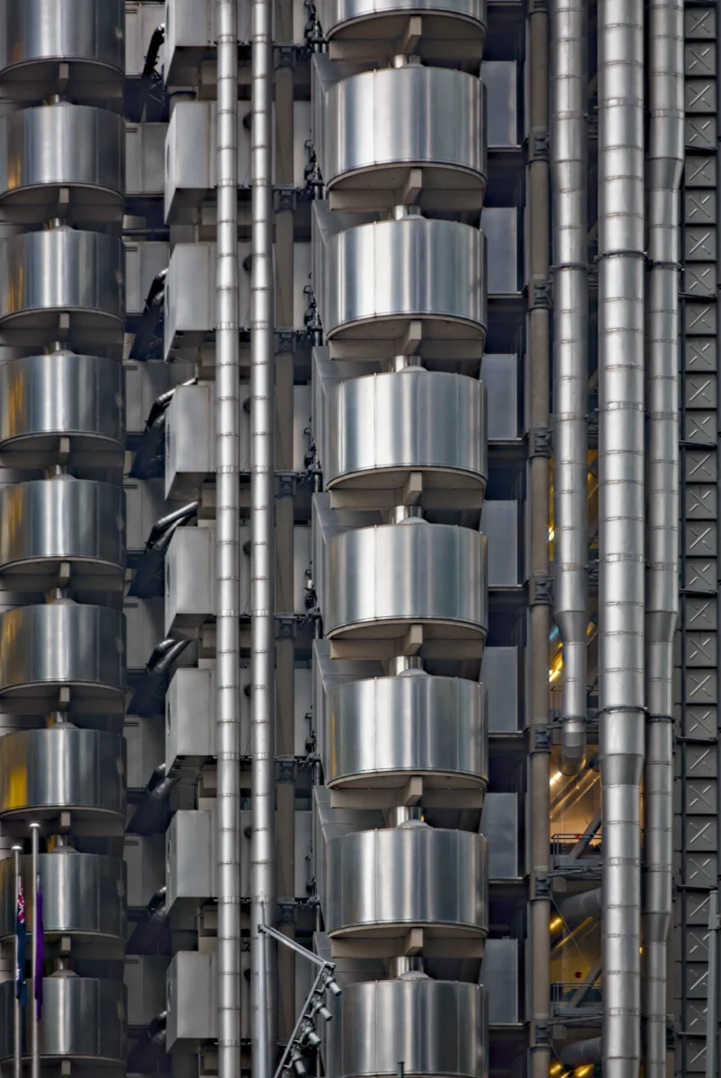 L'architecture mise à nu - Photographie d'art verticale du Lloyd's Building à Londres, gros plan sur les conduits métalliques et modules en acier.