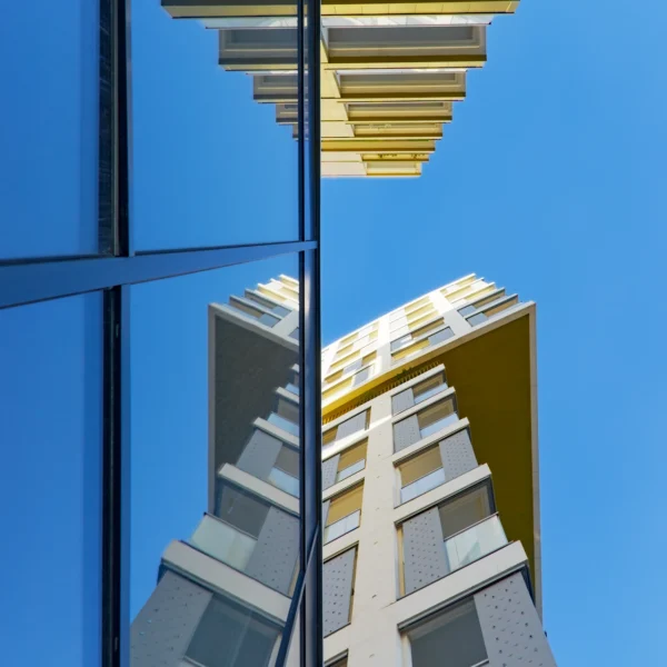 Photographie d'art en contre-plongée de la résidence Palomaya, montrant la façade blanche et or se reflétant symétriquement dans une paroi de verre noire face à un ciel bleu.