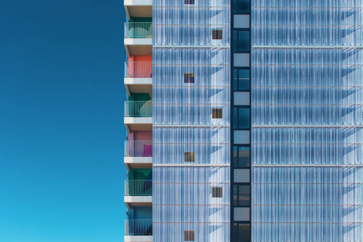 Photographie d'art de la résidence étudiante Anemone, montrant une façade en chaînes d'aluminium tressées scintillantes et des balcons colorés sur fond de ciel bleu.