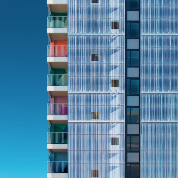 Photographie d'art de la résidence étudiante Anemone, montrant une façade en chaînes d'aluminium tressées scintillantes et des balcons colorés sur fond de ciel bleu.